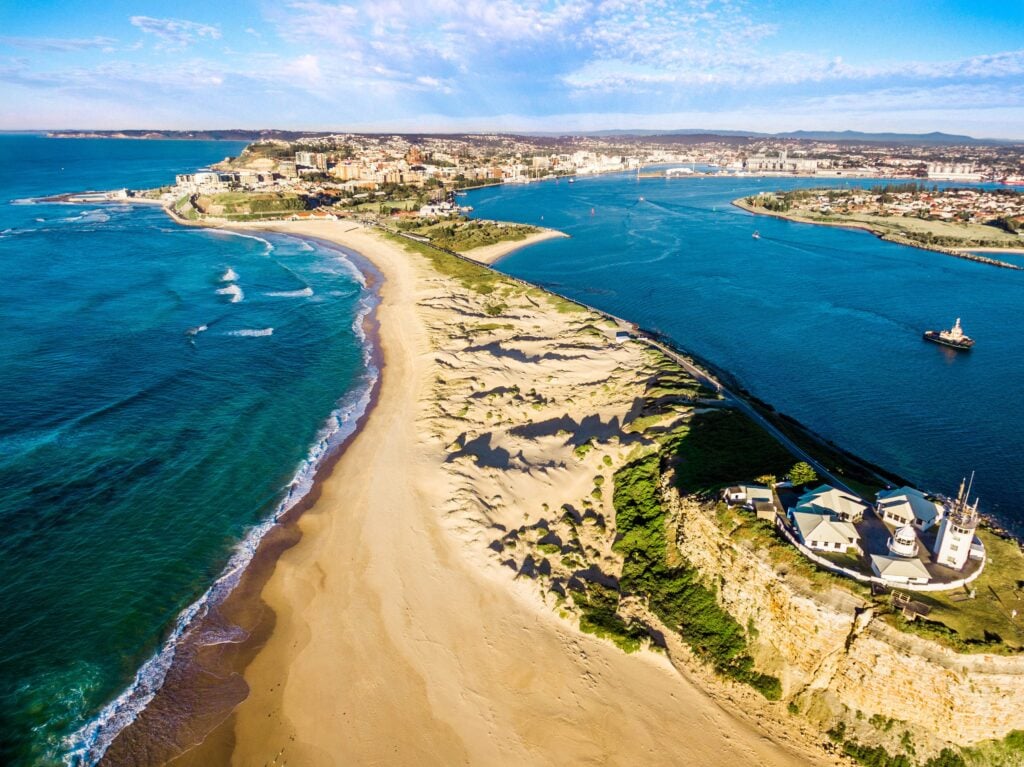 A Shartru Wealth aerial photo shows a beach peninsula with a lighthouse and a city.