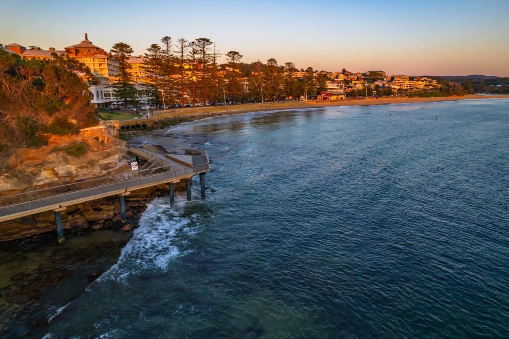 A Shartru Wealth photo shows a beach town at sunset with a walking path over the ocean.