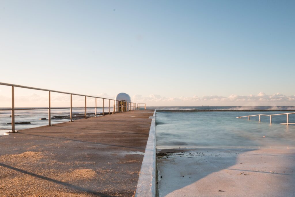 A Shartru Wealth photo shows a long ocean pool at sunset with a concrete walkway.