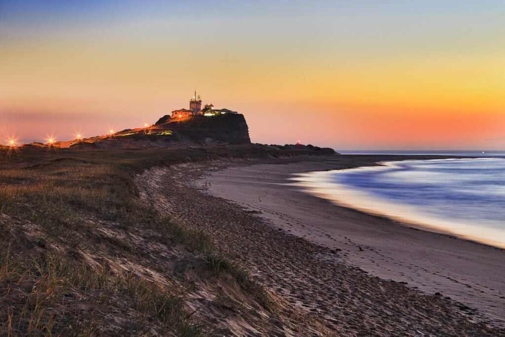 A photo from Shartru Wealth shows a lighthouse on a cliff at night.