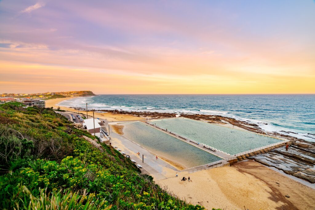 A Shartru Wealth photo of a coastline with ocean pools and a beach at sunset.