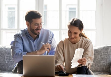 Shartru Wealth Management couple budgeting together with laptop, receipts, and calculator at home.