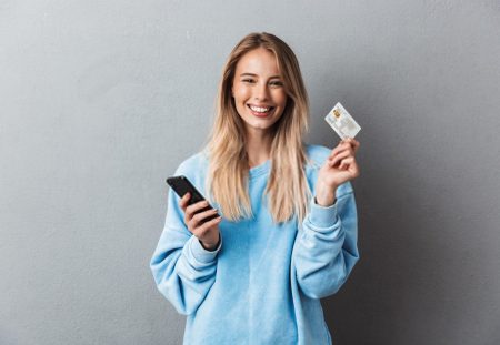 A smiling person from Shartru Wealth holds a credit card and a mobile phone.
