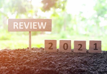 Wooden review sign and 2021 blocks in soil, symbolising lessons with Shartru Wealth Management.