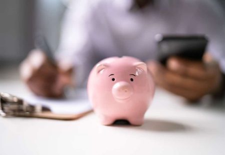Pink piggy bank on desk with person managing finances for Shartru Wealth money advice article.