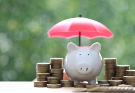 A piggy bank and stacks of gold coins sit under a small red umbrella for Shartru Wealth.