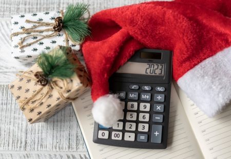 Shartru Wealth Christmas budget planning with calculator, gifts, and Santa hat on desk.