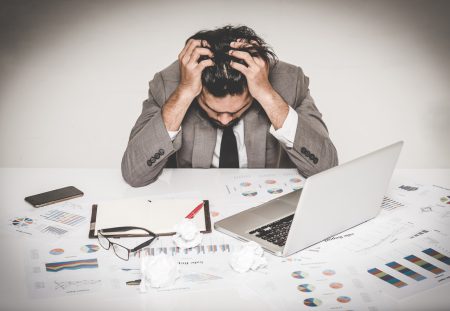 A Shartru Wealth client with their head in their hands sits at a desk with financial charts.