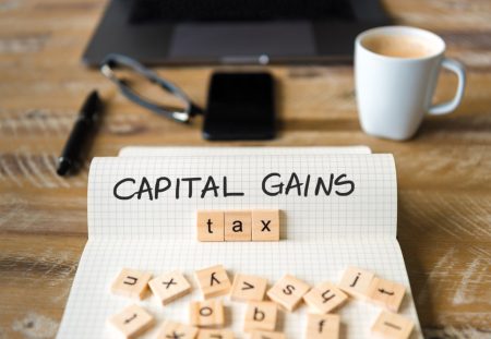 Capital gains tax written in notebook with letter tiles on desk, Shartru Wealth blog.