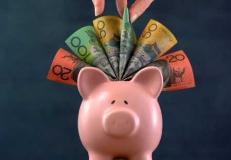 A person from Shartru Wealth holds a pink piggy bank with a fan of Australian money.
