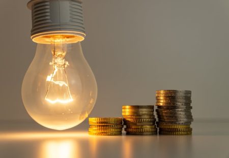 Glowing light bulb beside stacked coins symbolising energy savings, Shartru Wealth electricity bills blog.