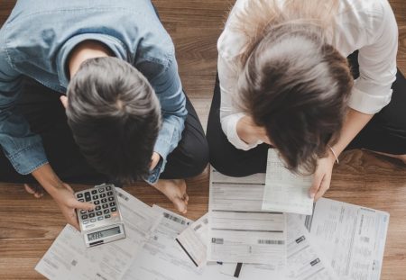 Shartru Wealth image of couple sitting on floor with calculator and bills spread out around them.