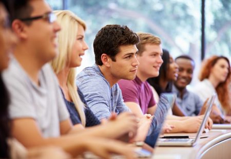 Shartru Wealth shows university students sitting in lecture hall with laptops.