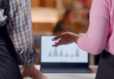 Two colleagues reviewing employee share performance charts on laptop, discussing tax impacts with Shartru Wealth Management.