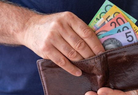A close-up from Shartru Wealth shows a person's hands pulling Australian money from a wallet.