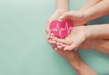 Shartru Wealth image of hands holding red heart with heartbeat symbol representing health insurance costs.