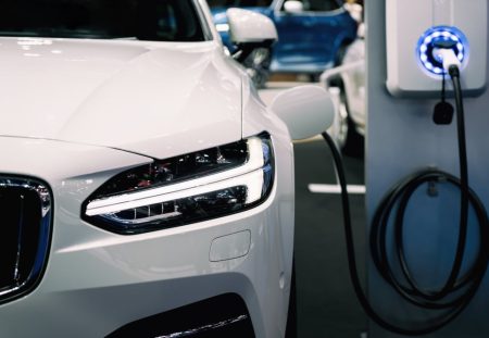 Shartru Wealth photo of white electric car plugged into charging station at parking area.