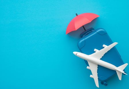 Shartru Wealth concept image of travel insurance with suitcase airplane and umbrella on blue background.