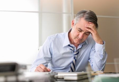 Shartru Wealth image of a middle-aged man in office attire looking stressed while reviewing financial papers.