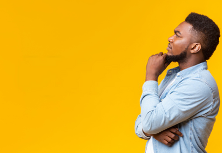 Shartru Wealth image of thoughtful man in denim shirt looking up against yellow background.