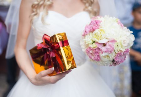 Shartru Wealth image of bride holding pink wedding bouquet and golden wrapped gift box.