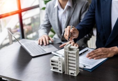 Shartru Wealth advisers reviewing property contracts with model buildings on desk.