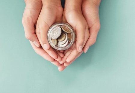 Shartru Wealth child and parent holding a jar of coins together.