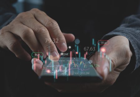 A Shartru Wealth client holds a mobile phone with a stock market chart on the screen.
