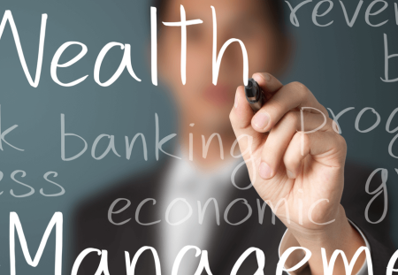 A person's hand from Shartru Wealth writes the words "Wealth Management" on a clear board.