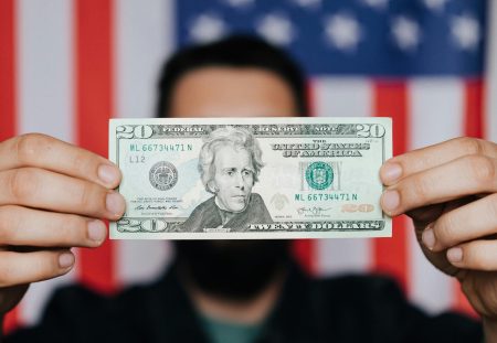 Hands holding a US twenty dollar note before an American flag, in a Shartru Wealth article.